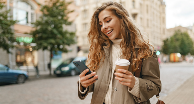 mujer en la calle con un teléfono y café en la mano
